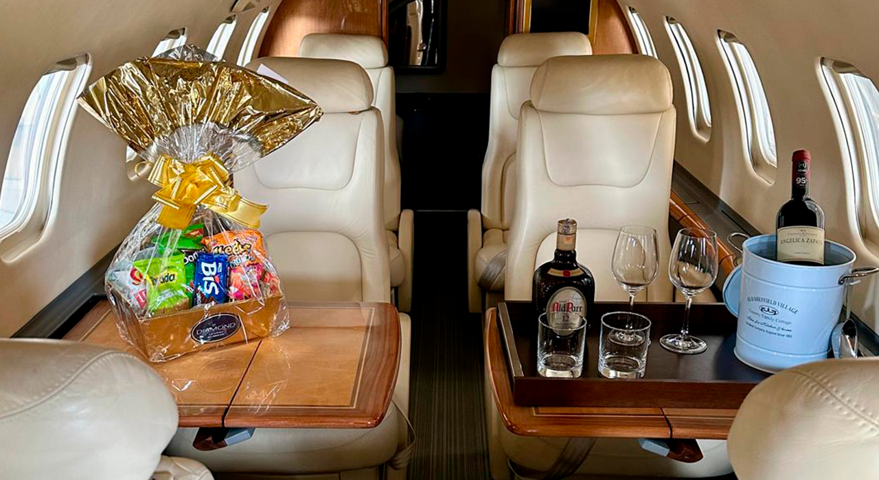 Interior de aeronave executiva preparada para voo fretado, com poltronas de couro, mesa de apoio e serviço de bordo para maior conforto dos passageiros.